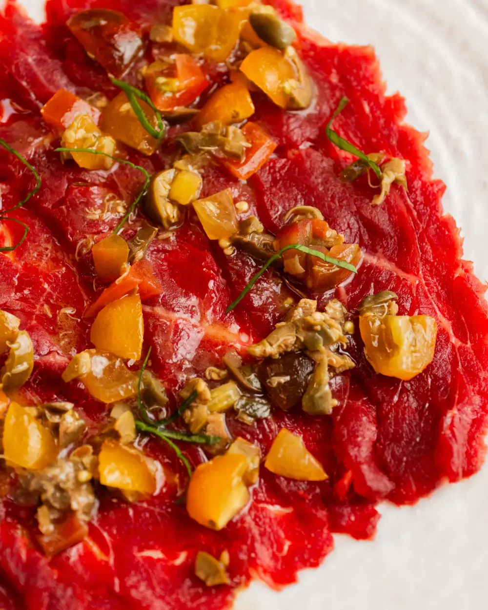 Carpaccio di manzo alla mediterranea con datterini e olive su piatto bianco