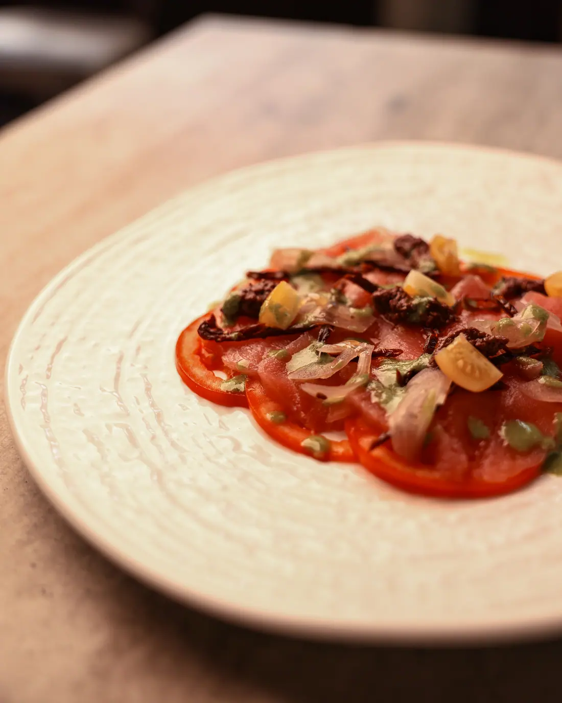 Carpaccio di pomodoro cuore di bue con datterini gialli e olive su piatto bianco