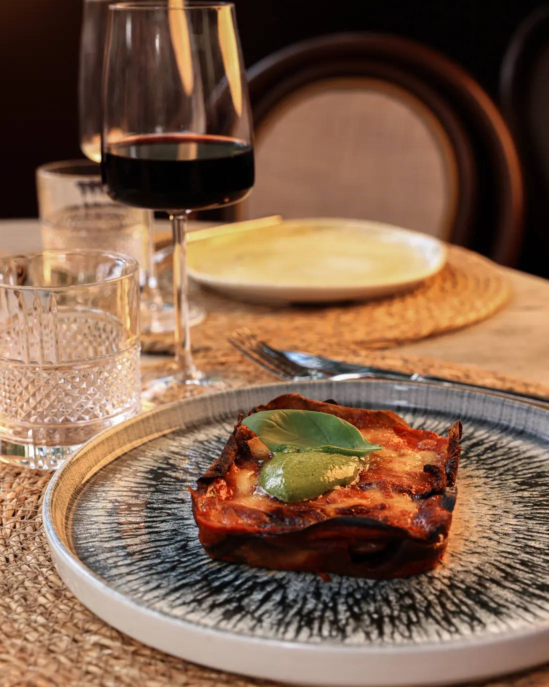 Parmigiana di melanzane con foglia di basilico e pesto su piatto decorato
