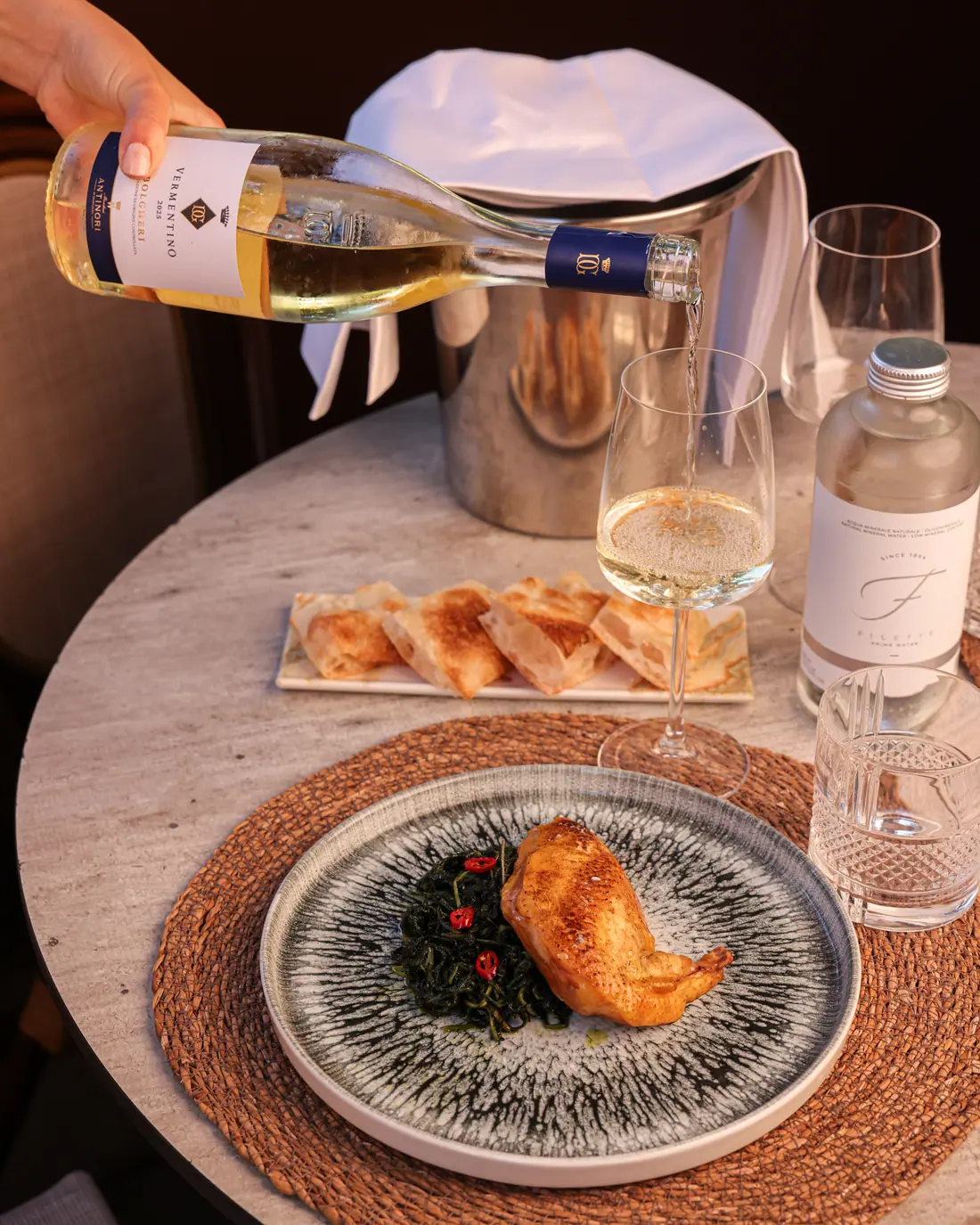 Tavola apparecchiata con vino bianco in secchiello, focaccine e piatto di suprema di pollo